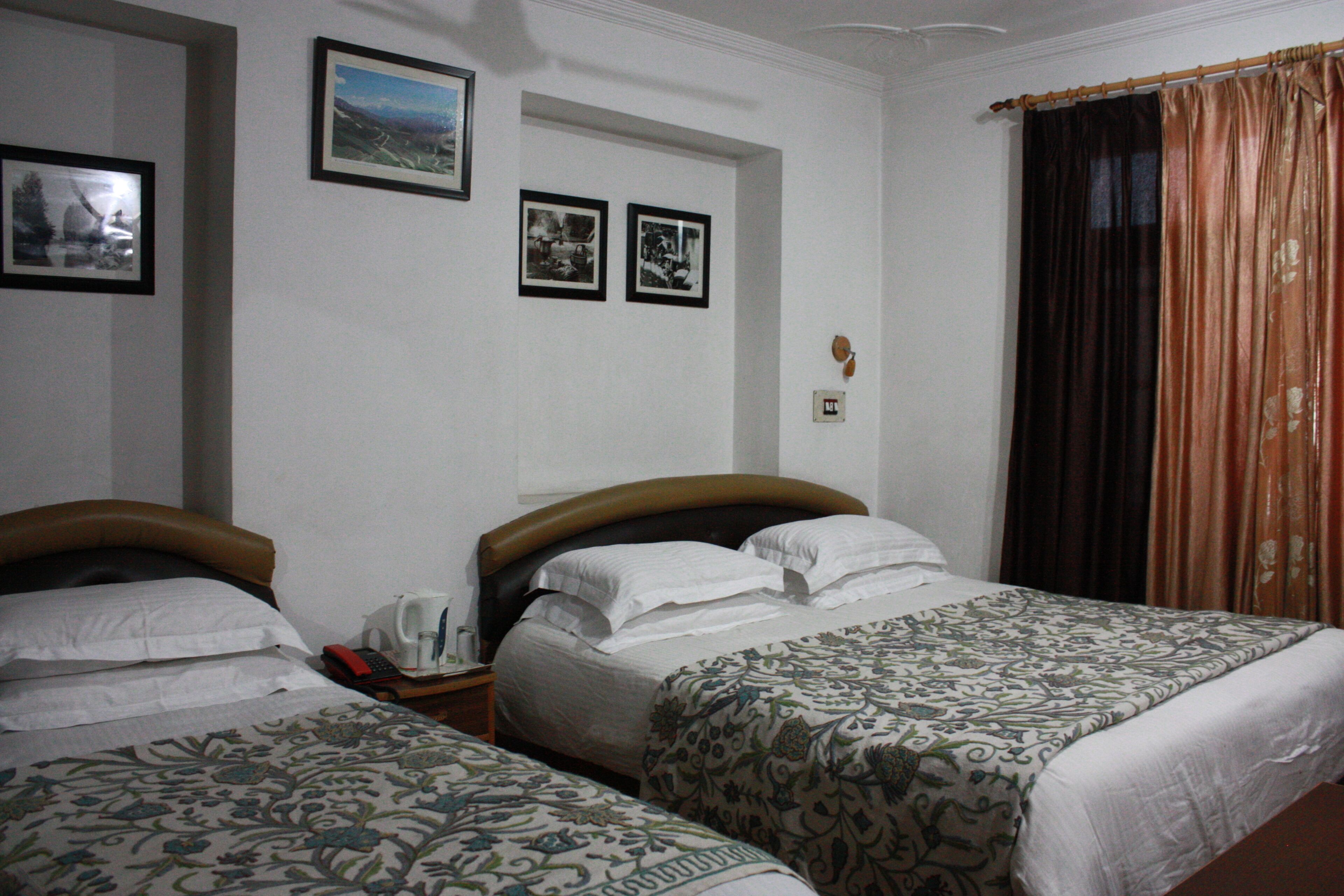 A hotel room with two beds, a nightstand with a telephone, and framed pictures on the wall.