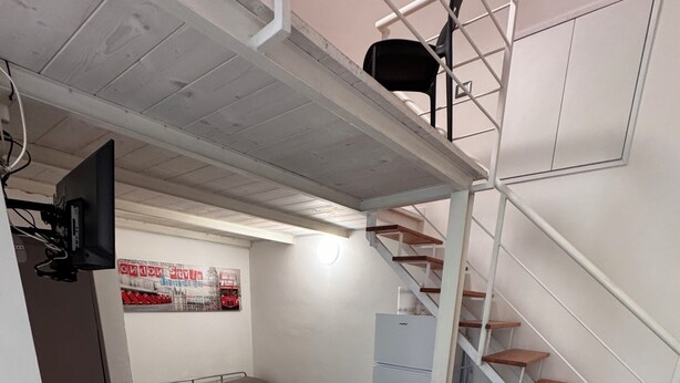 Una habitación compacta con una mesa de comedor, sillas, un sofá, una pequeña cocina y una escalera.