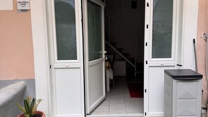 Fachada de edificio con puerta blanca, una planta en maceta y un mueble bajo.