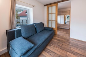 Una habitación moderna con un sofá azul oscuro, piso de madera y una puerta corredera de vidrio que da a un espacio al aire libre.