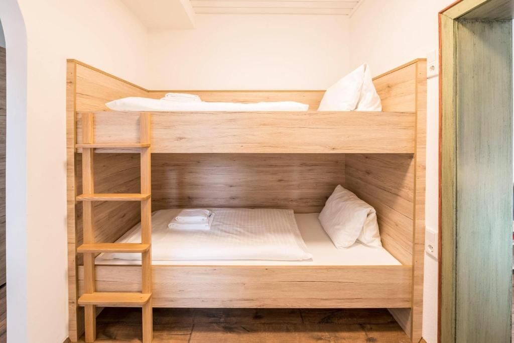 A bunk bed with a wooden ladder, white bedding, and a wooden headboard.