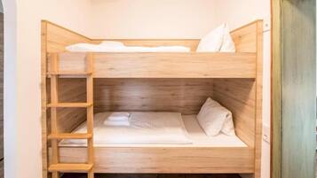 A bunk bed with a wooden ladder, white bedding, and a wooden headboard.