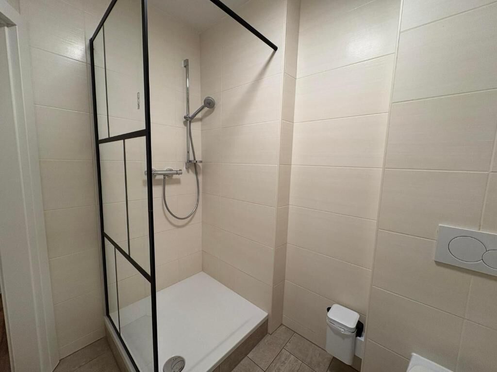 A small, enclosed shower area with a glass partition, a white bathtub, and a white toilet.