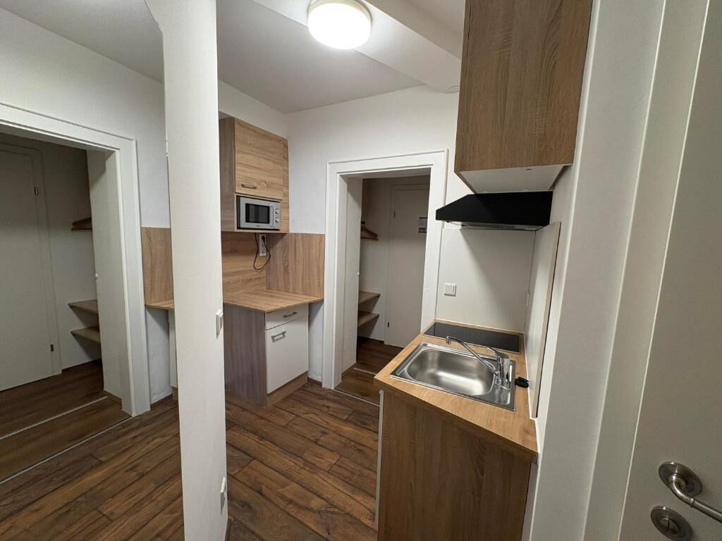 A compact kitchen with a microwave, sink, and wooden cabinets.