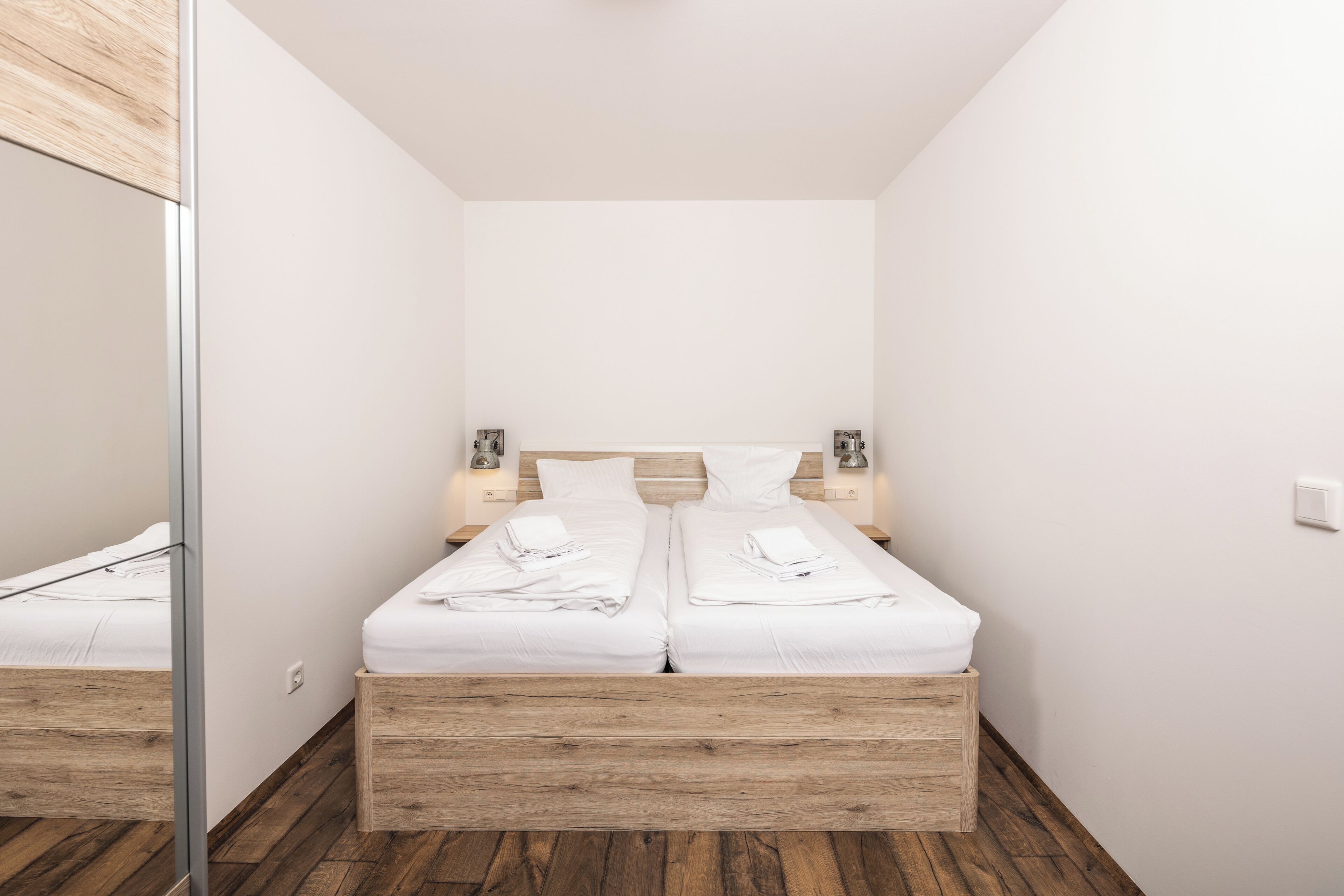 Ein modernes Schlafzimmer mit einem Bettgestell aus Holz, weißer Bettwäsche und Nachttischlampen.