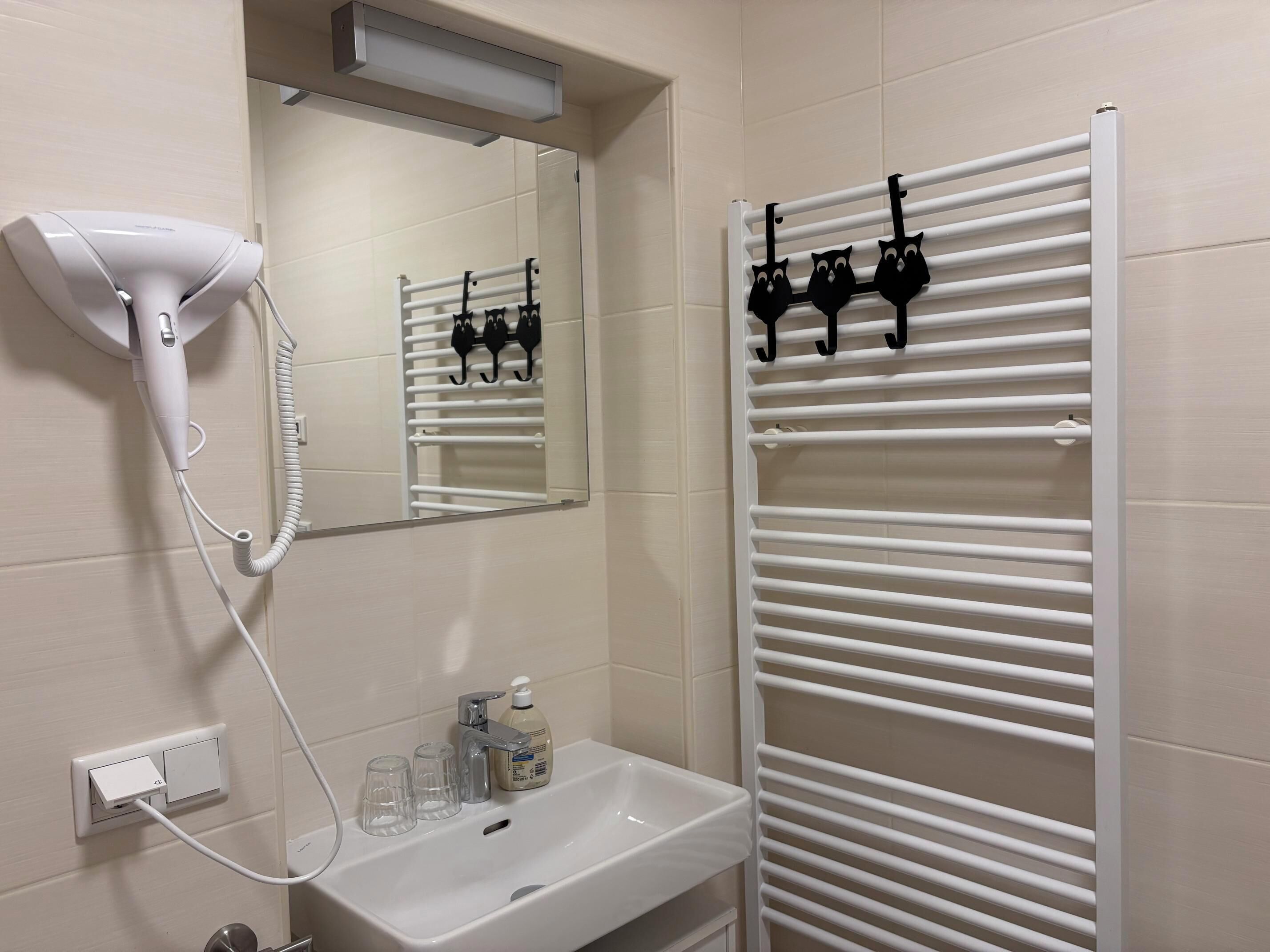 A bathroom with a hairdryer, a mirror, a sink with glasses and soap, and a towel rack.
