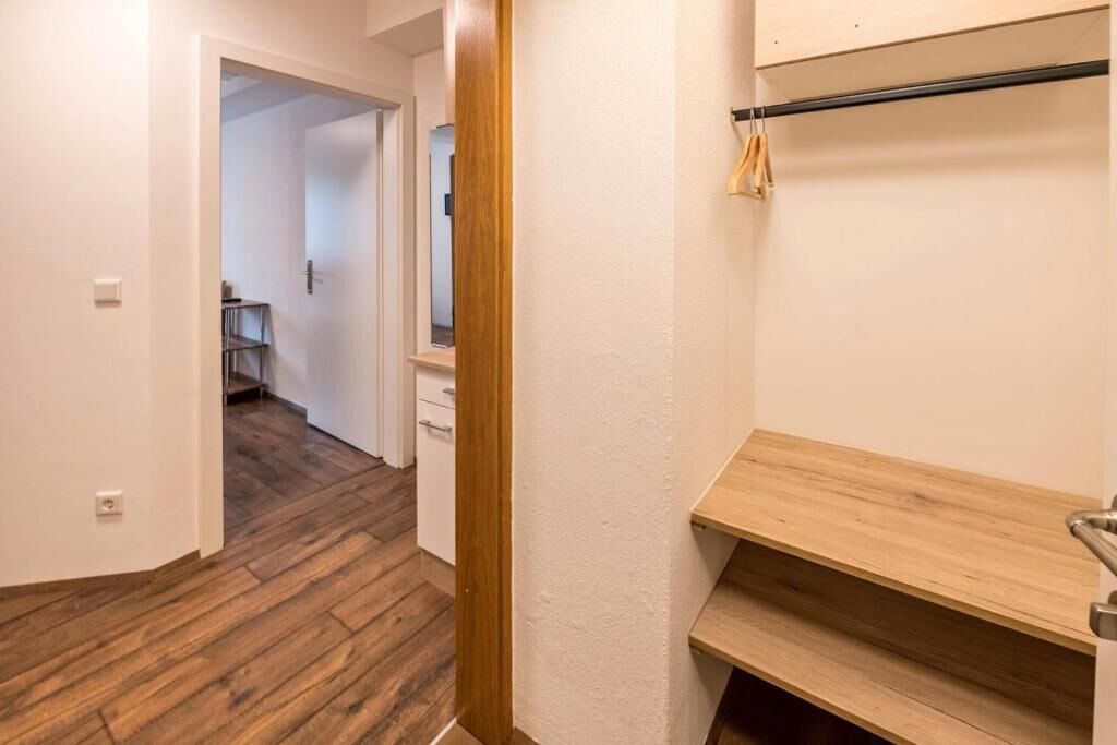 A hallway with wooden flooring, a white door, and a wooden bench with a towel rack.
