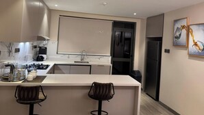A modern kitchen with a marble backsplash, stainless steel appliances, and two bar stools. - Apartments at Abrish by Karibu Stays (Kampala)