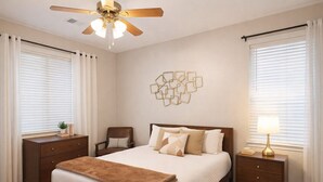 Una camera da letto con un letto, comodini, una poltrona, una ventola a soffitto e un quadro appeso al muro.