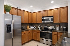 Una cocina moderna con armarios de madera, electrodomésticos de acero inoxidable, un microondas integrado y un dispensador de agua.