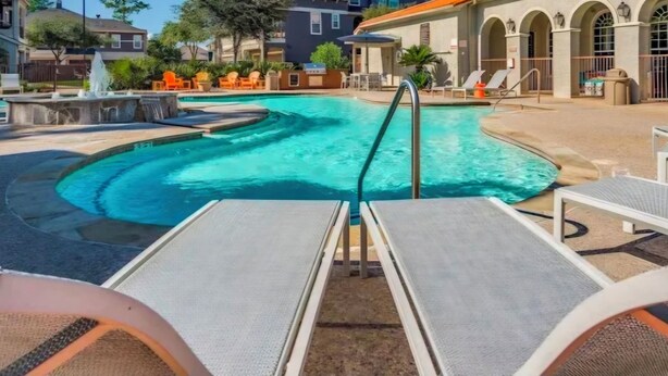 Una piscina con lettini, una fontana e un edificio con archi sullo sfondo.