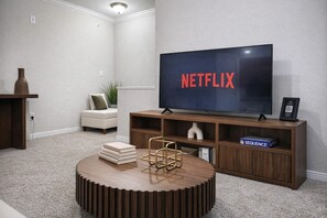 Ein Wohnzimmer mit einem großen Flachbildfernseher, einem runden Couchtisch, einem Bücherregal und einer Couch.
