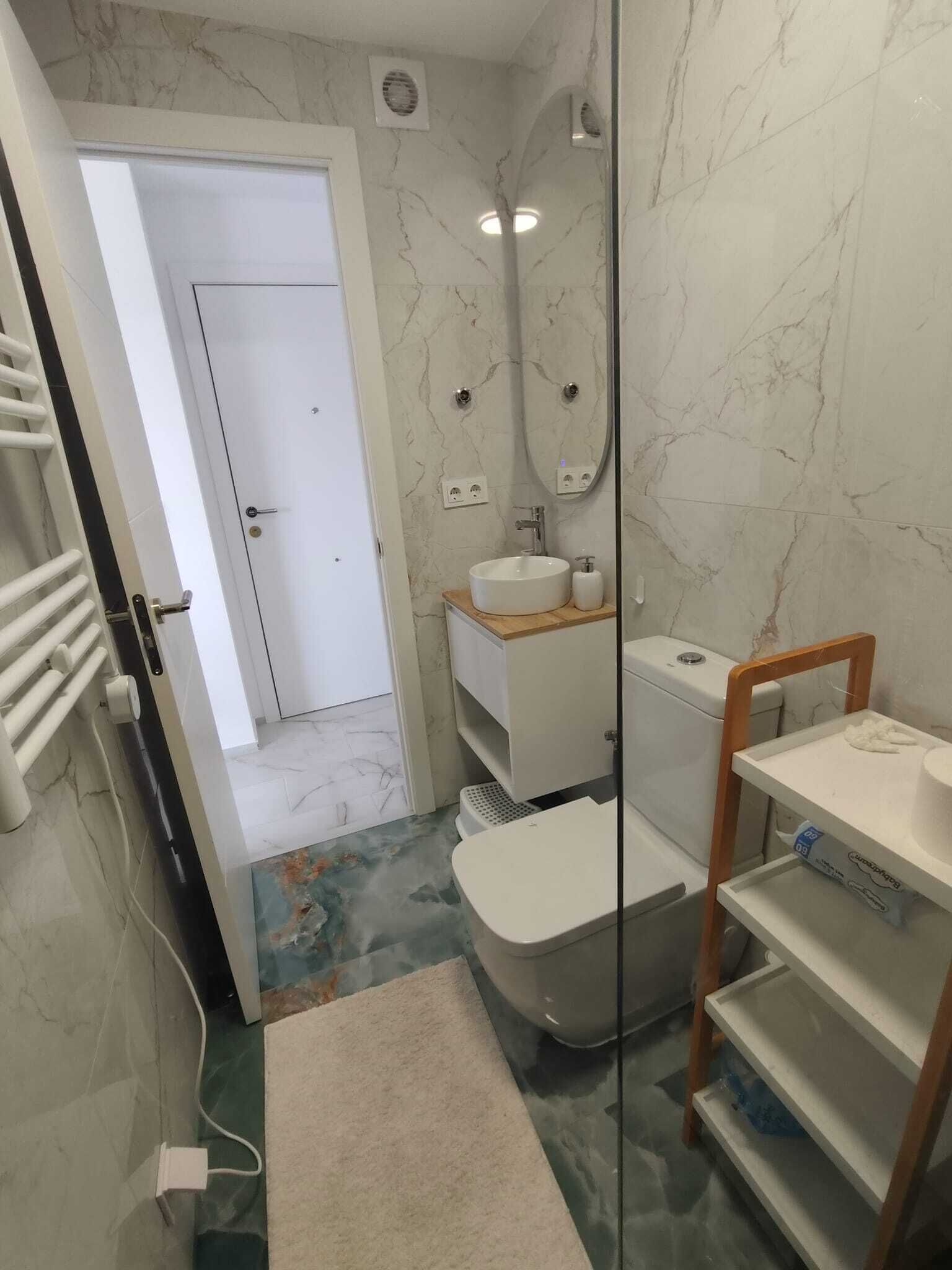 A bathroom with a white sink, mirror, and a shower area. There is a towel rack and a shelf with toiletries.