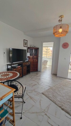 A living room with a TV, wooden cabinet, and a dining area with a table and chairs.