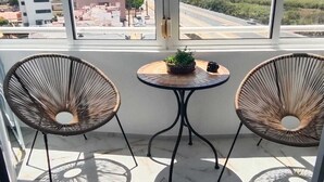 A balcony with two wicker chairs, a small round table with a plant and a cup, and a view of buildings and a road. - Bright one bedroom apartment in La Mata, Avenida Suiza. With pool. (La Mata)