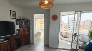 A living room with a TV, wooden cabinet, and a large window. - Bright one bedroom apartment in La Mata, Avenida Suiza. With pool. (La Mata)