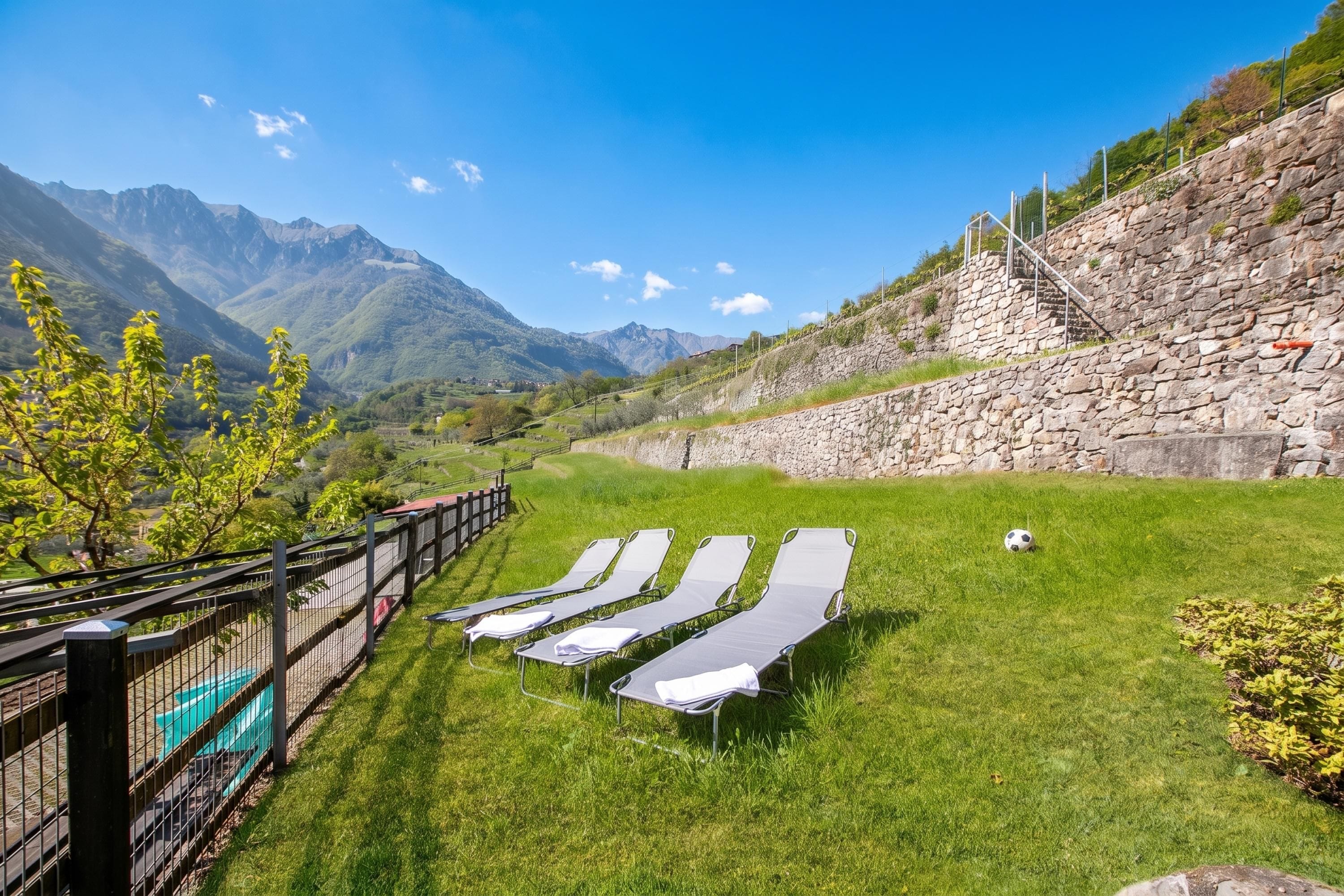 Zona verde con sillones de descanso y un muro de piedra, con vista a un paisaje montañoso.