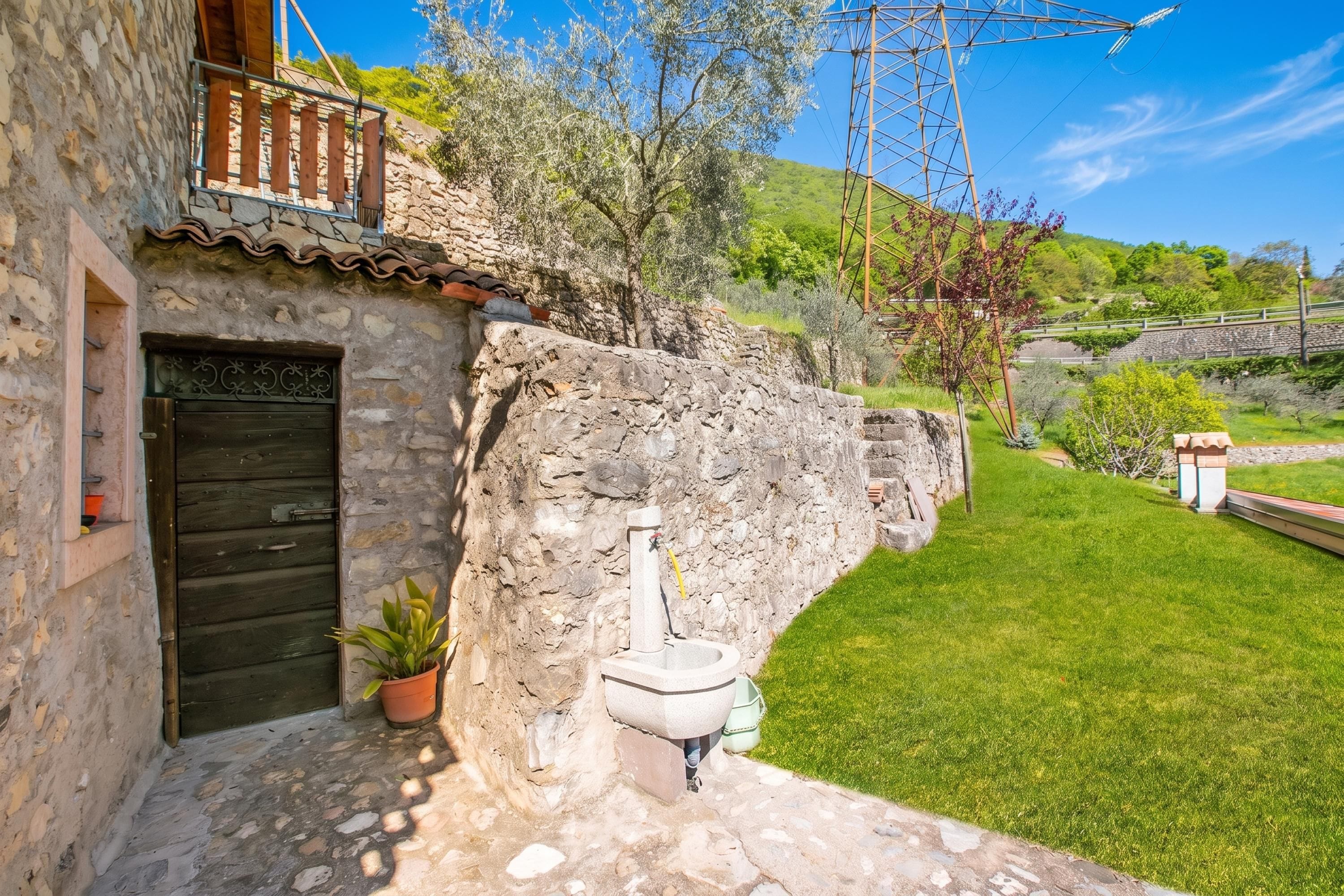 A stone house with a wooden door, a small balcony, and a stone wall.