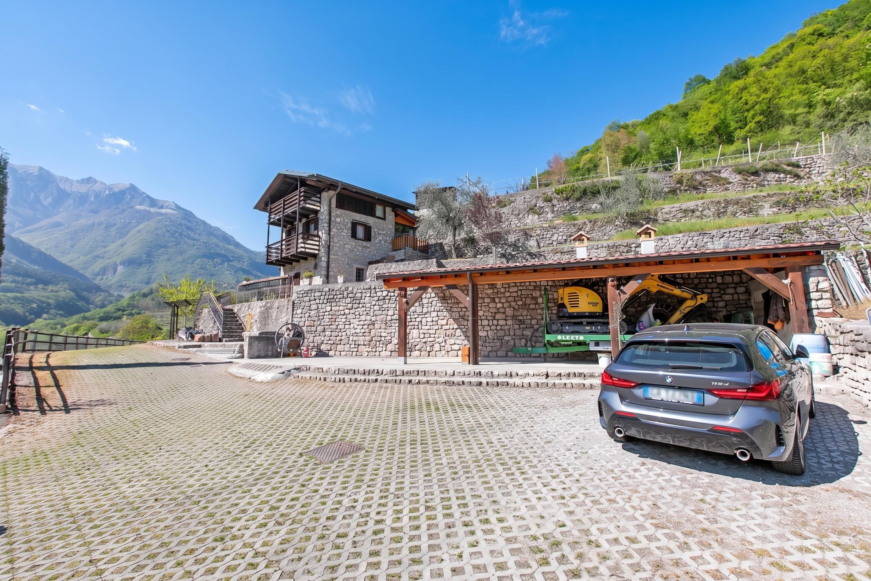 Un edificio de piedra con balcón, un coche estacionado al frente y montañas al fondo.