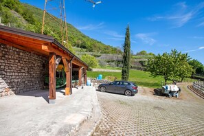 A stone building with a wooden roof, a parked car, and a paved area with a tree and a fence. - Private Green Oasis - Terrace (Tenno)