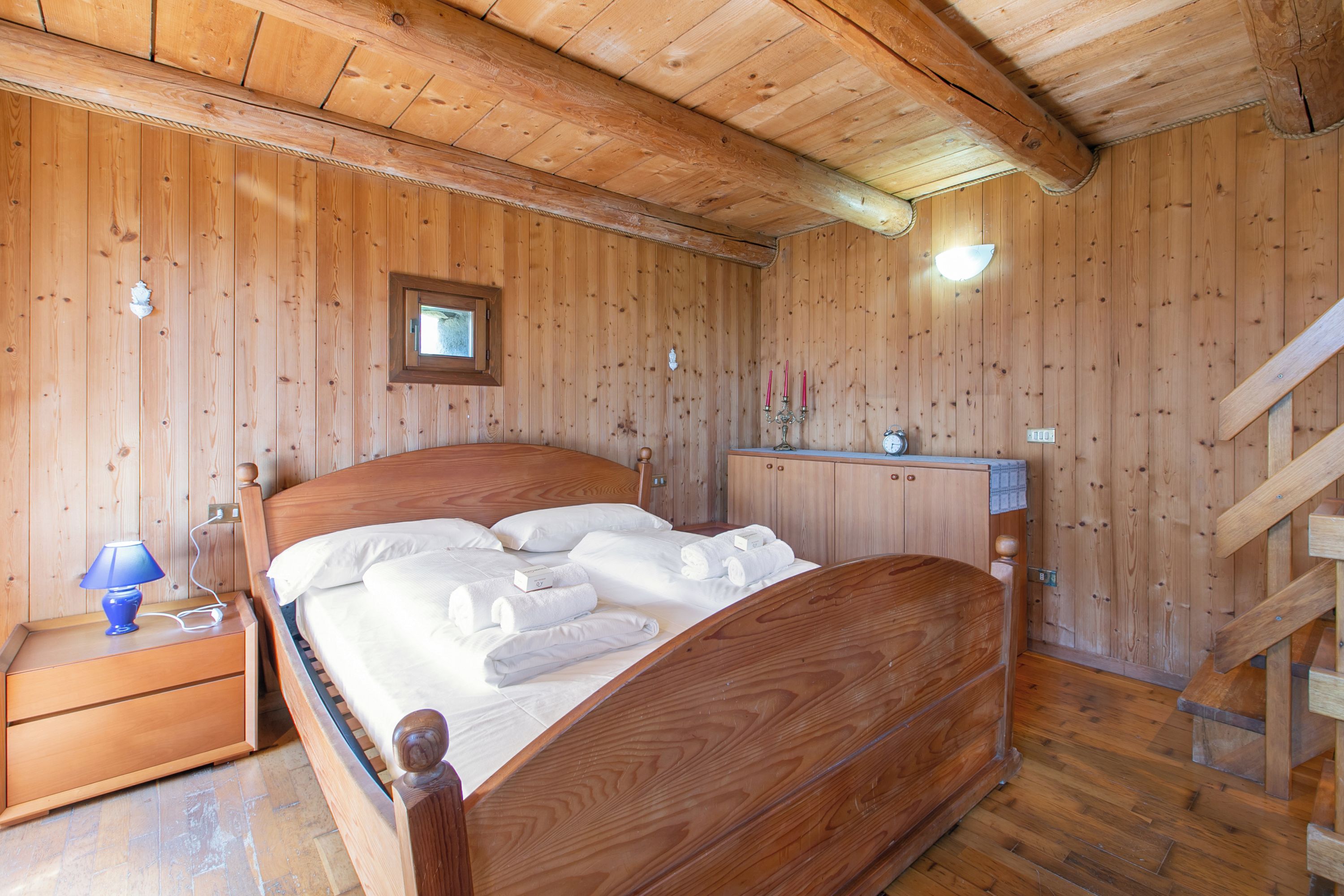 Una habitación con paneles de madera, una cama, una mesita de noche, un aparador y una escalera.