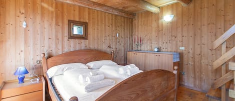 Una habitación con paneles de madera, una cama, una mesita de noche, un aparador y una escalera.