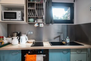 A compact kitchen with a microwave, kettle, sink, and storage cabinets. - Holiday Home 'P'tite Maizoun - Gîte' with Terrace, Garden and Wi-Fi (Hermanville-sur-Mer)