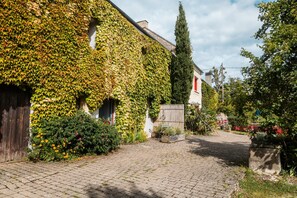 Un edificio con muros cubiertos de hiedra, un camino empedrado y un jardín con flores.