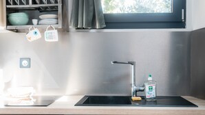 Eine Küche mit Spüle aus Edelstahl, einem Fenster darüber und einem Geschirrgestell mit Tassen und Schüsseln.