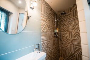 A bathroom with a mirror, sink, shower, and patterned tiles.