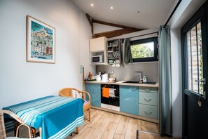 A compact kitchen with a dining area, featuring a table with a striped tablecloth, a microwave, a kettle, and a window with curtains.