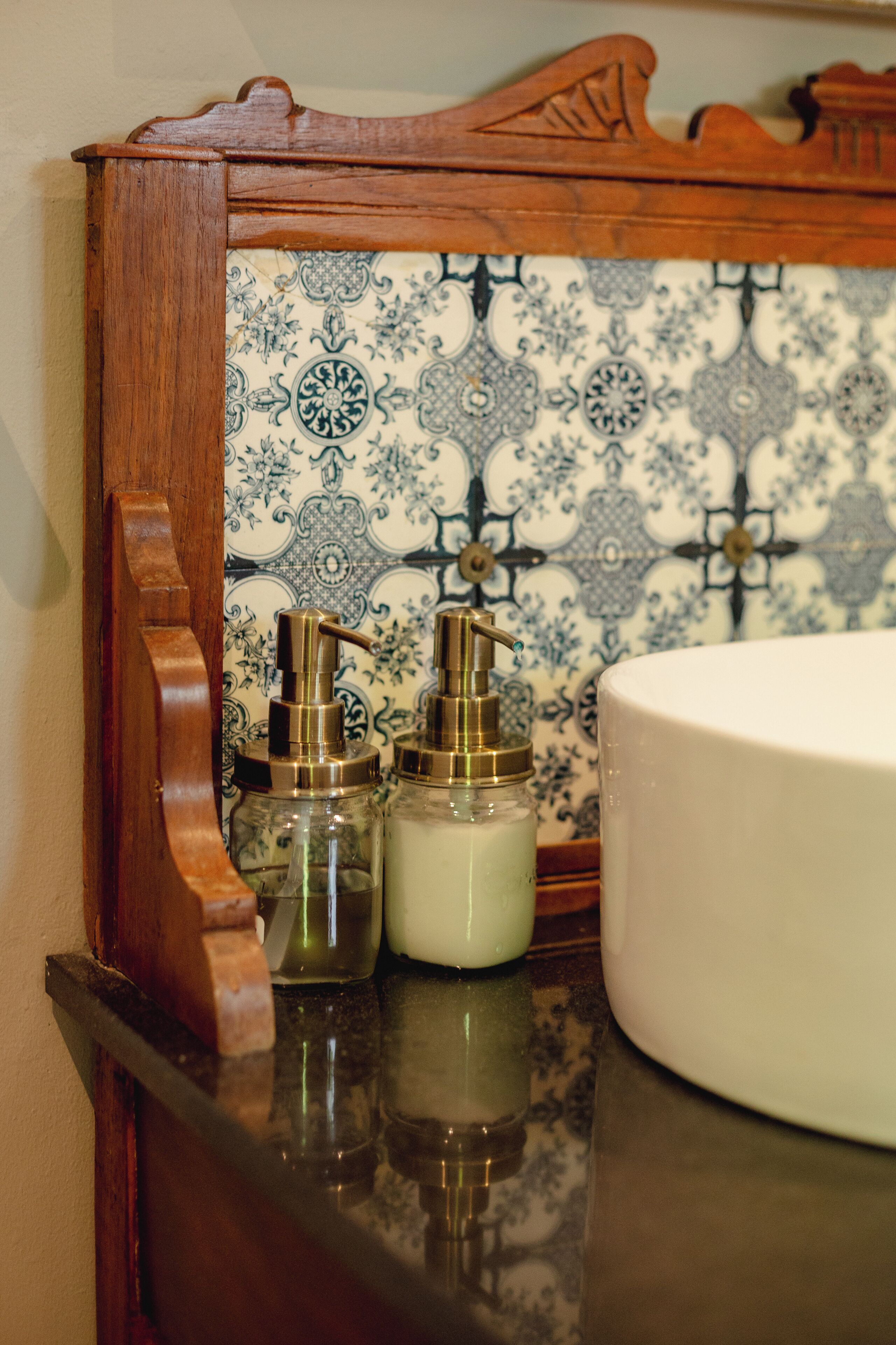 A bathroom with a white sink, two glass dispensers, and a patterned tile backsplash.