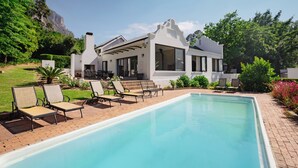 A modern house with a swimming pool, outdoor seating, and a mountain backdrop. - Hemelberg Guesthouse (Stellenbosch)