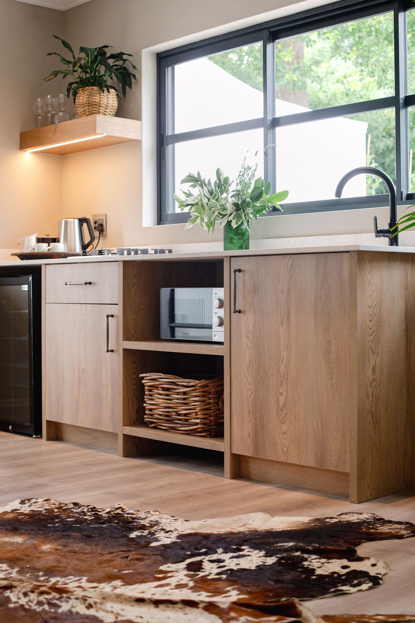 A modern kitchen with wooden cabinets, a microwave, a sink, and a window with a view of greenery.
