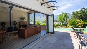 A modern living room with a large window, a fireplace, and a view of a mountain landscape. - Hemelberg Guesthouse (Stellenbosch)