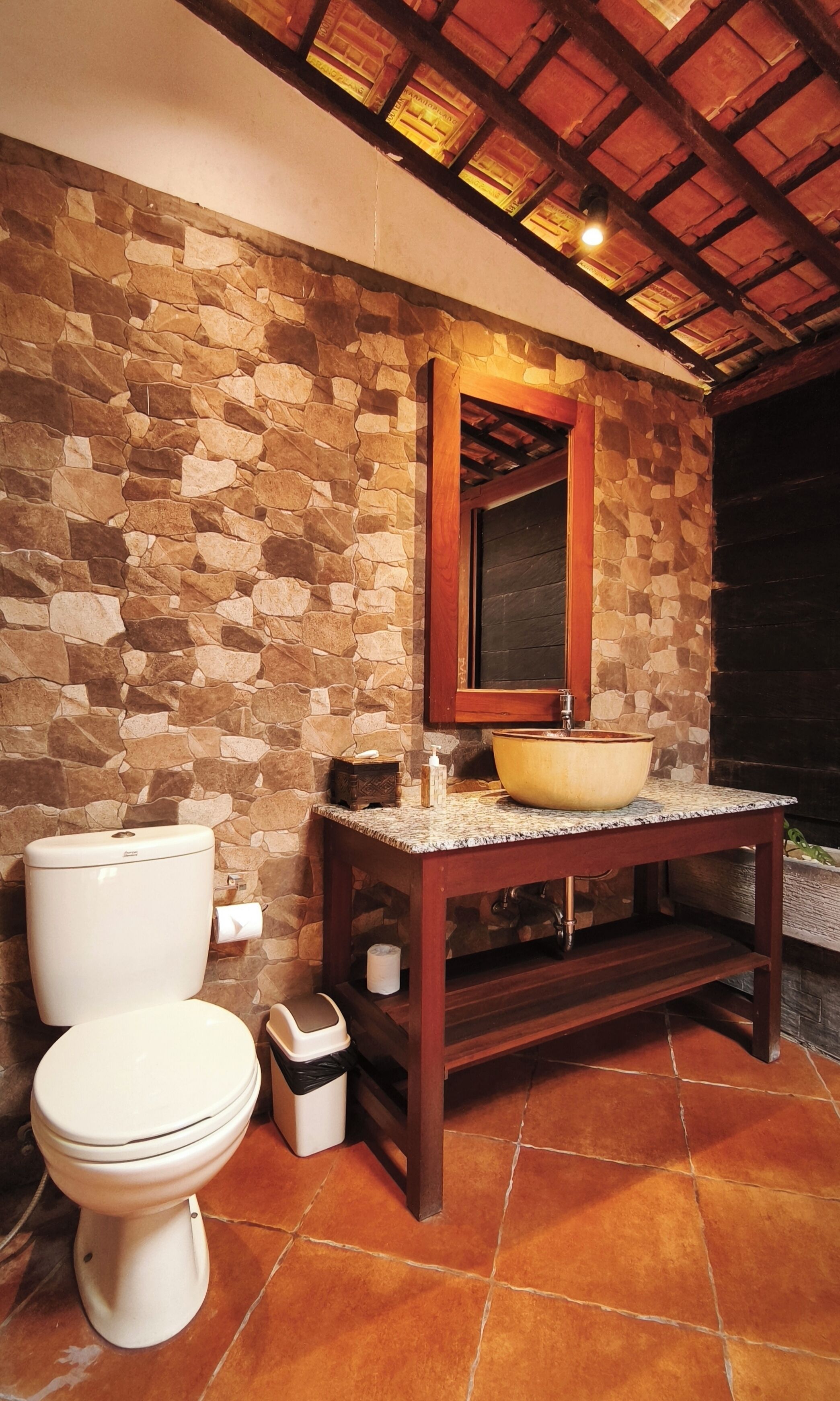 Un bany amb paret de pedra, un lavabo de fusta, un gran banyera-rentapisa, un vàter i un gresol.