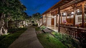 A pathway leading to a traditional wooden structure with a covered porch and a well-lit entrance.
