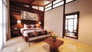 A hotel room with a wooden bed, bedside lamps, a sofa, a wooden coffee table, and a large window.
