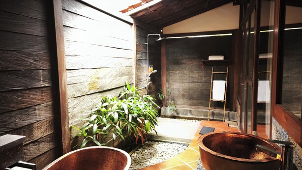 A wooden exterior with a small garden area, a metal shower, and a tiled floor.