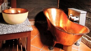 A rustic bathroom with a wooden bench, a copper basin, and a stone sink.