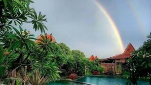 A pool area with a rainbow, surrounded by lush greenery and traditional architecture.
