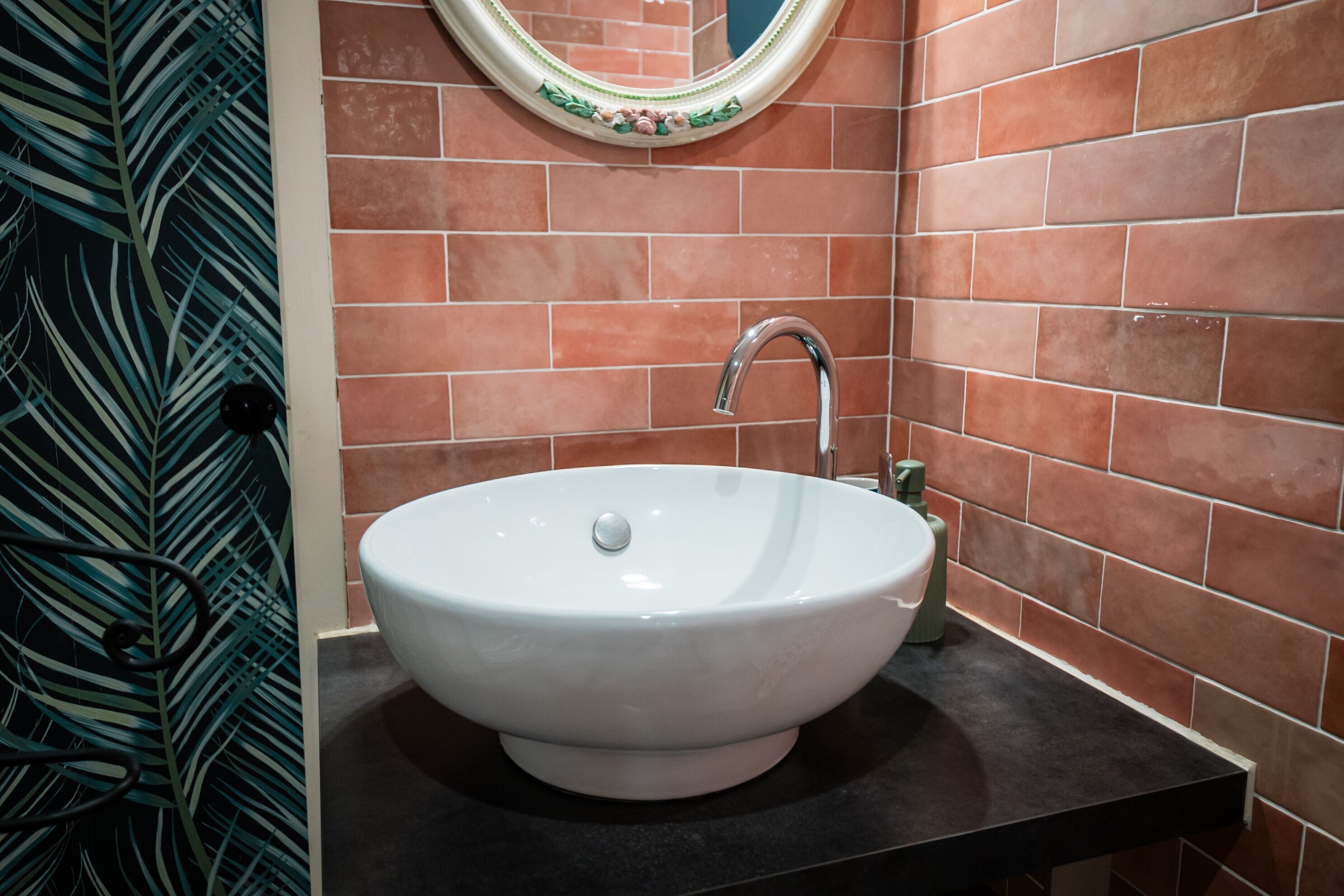 Une salle de bain avec un lavabo blanc, un plan de toilette noir et un miroir doté d’un cadre décoratif.