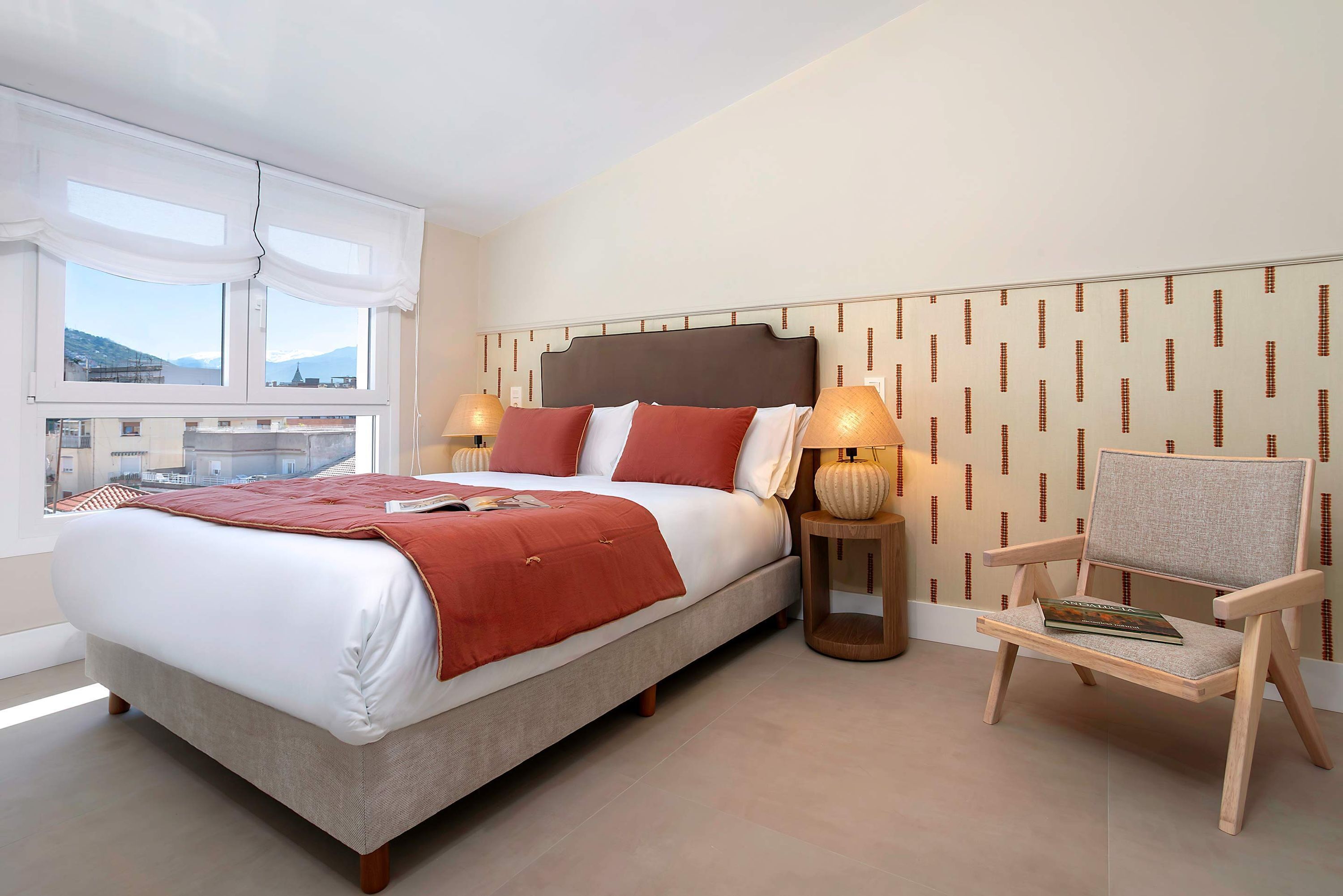 Een slaapkamer met een bed, twee bedlampen, een stoel en uitzicht op buiten.