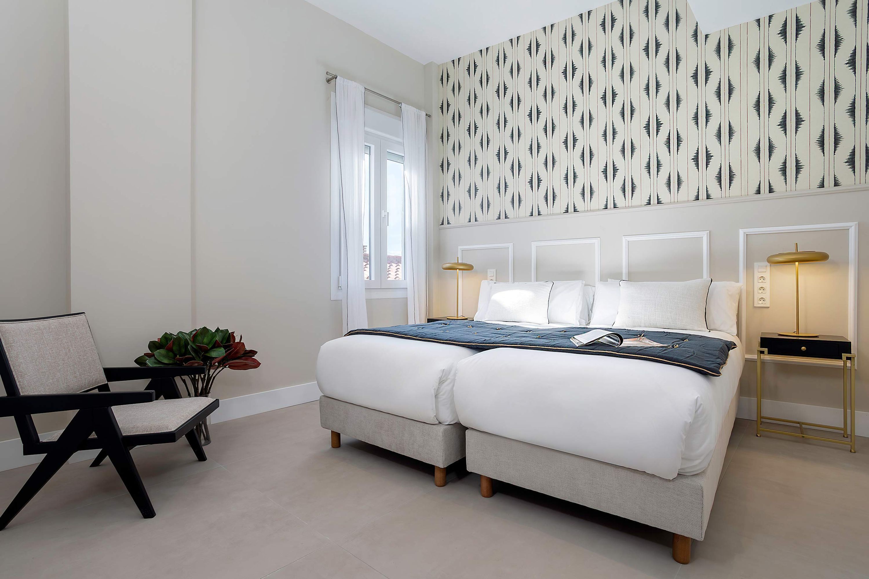 A bedroom with a bed, a chair, a bedside table, and a window.