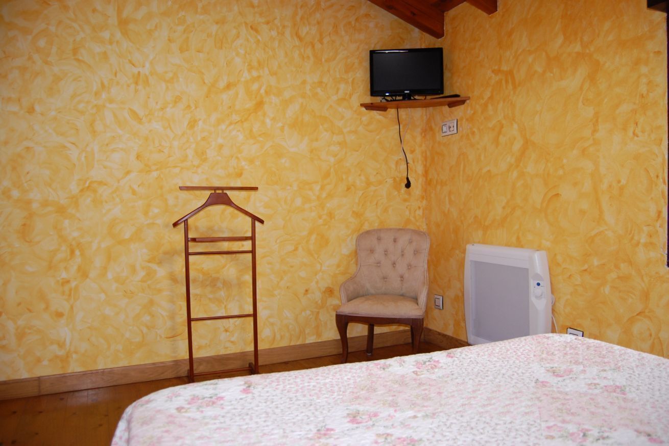 Une pièce comprenant un lit, une chaise, un téléviseur fixé au mur et un petit appareil électroménager blanc.