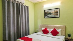 Habitación de hotel con una cama, cortinas grises, aire acondicionado de pared, un cuadro enmarcado y una pequeña planta en maceta.