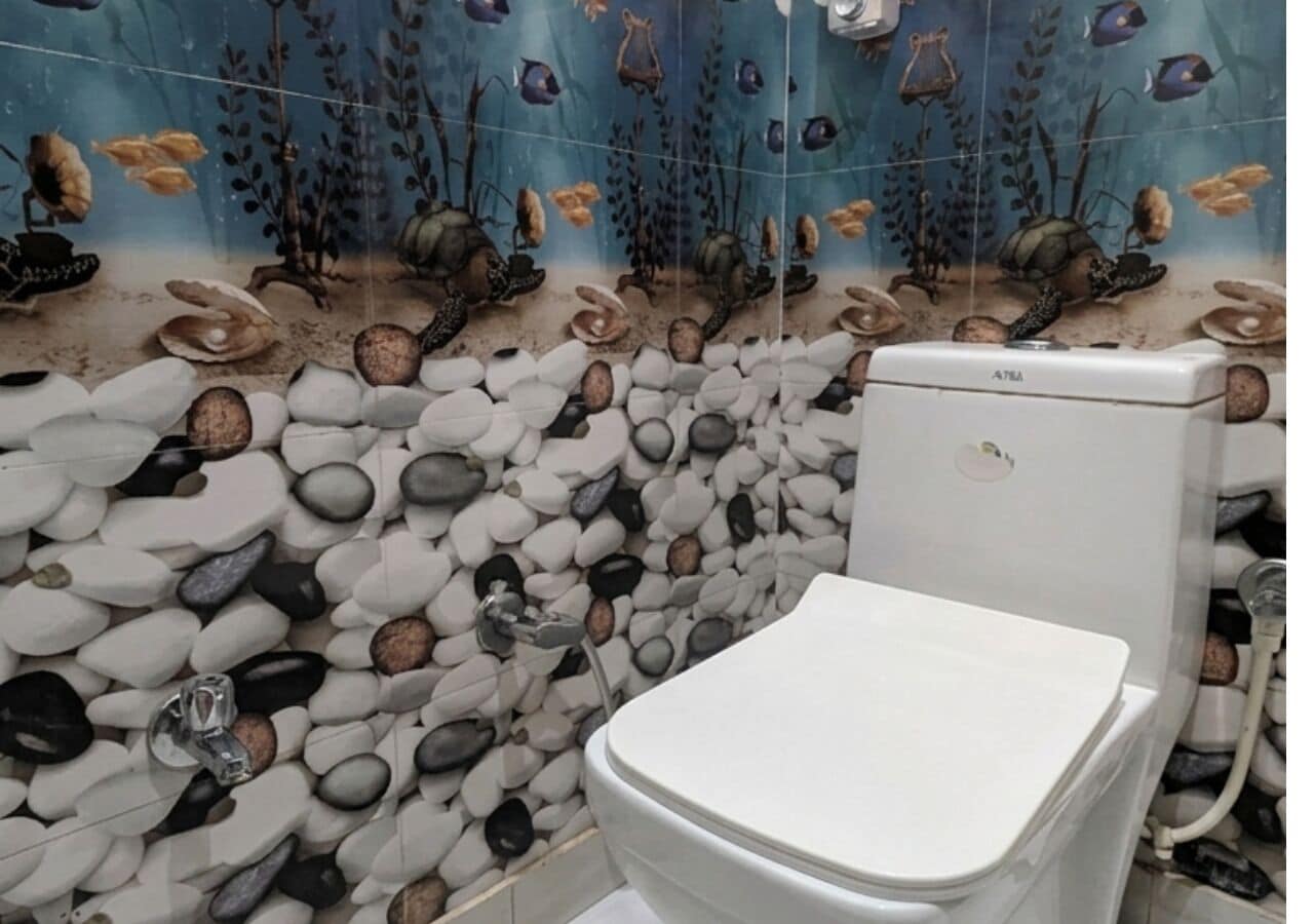 A bathroom with a toilet, pebbles, and an underwater mural.