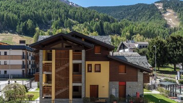 Un edificio de varios pisos con balcones, fachada de piedra y montañas al fondo.