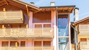 A multi-story building with wooden balconies, a glass elevator, and a stone chimney. - Tana dell'Elfo Palú (Aprica)