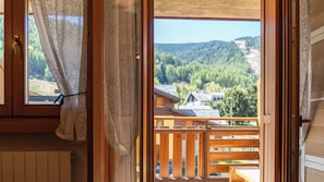A wooden balcony with a view of a forested valley and a house. - Tana dell'Elfo Palú (Aprica)
